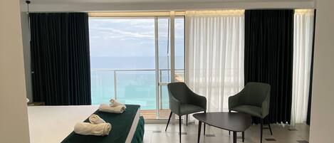 Habitación de hotel con cama, dos sillas, una mesita y vista al mar.