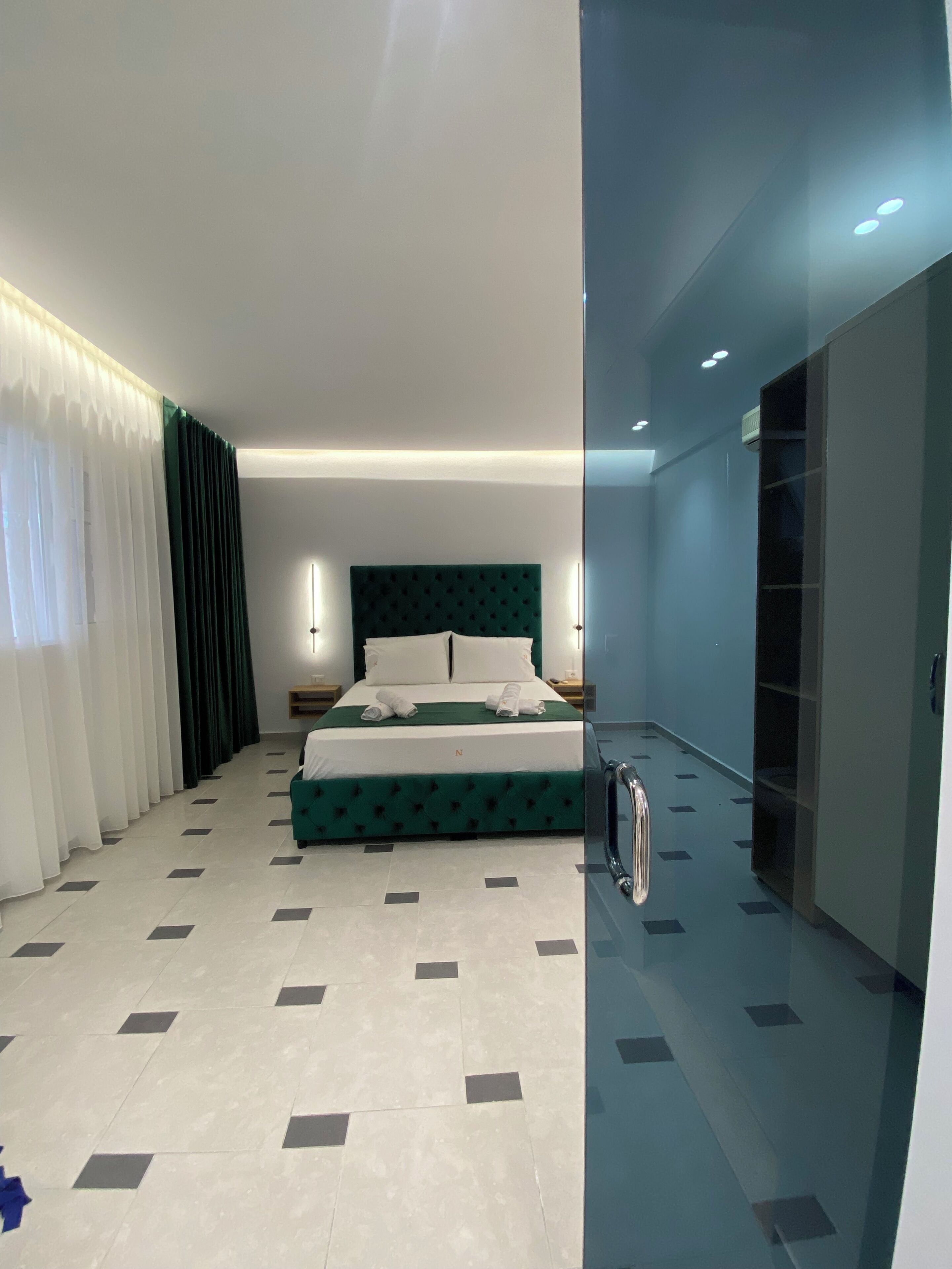 Una moderna camera d'albergo con un letto grande, un comodino e un tavolino. È presente una parete divisoria in vetro su un lato della stanza.