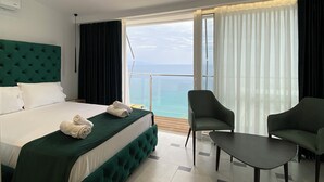 A hotel room with a large bed, two armchairs, a small table, and a balcony with a view of the sea.