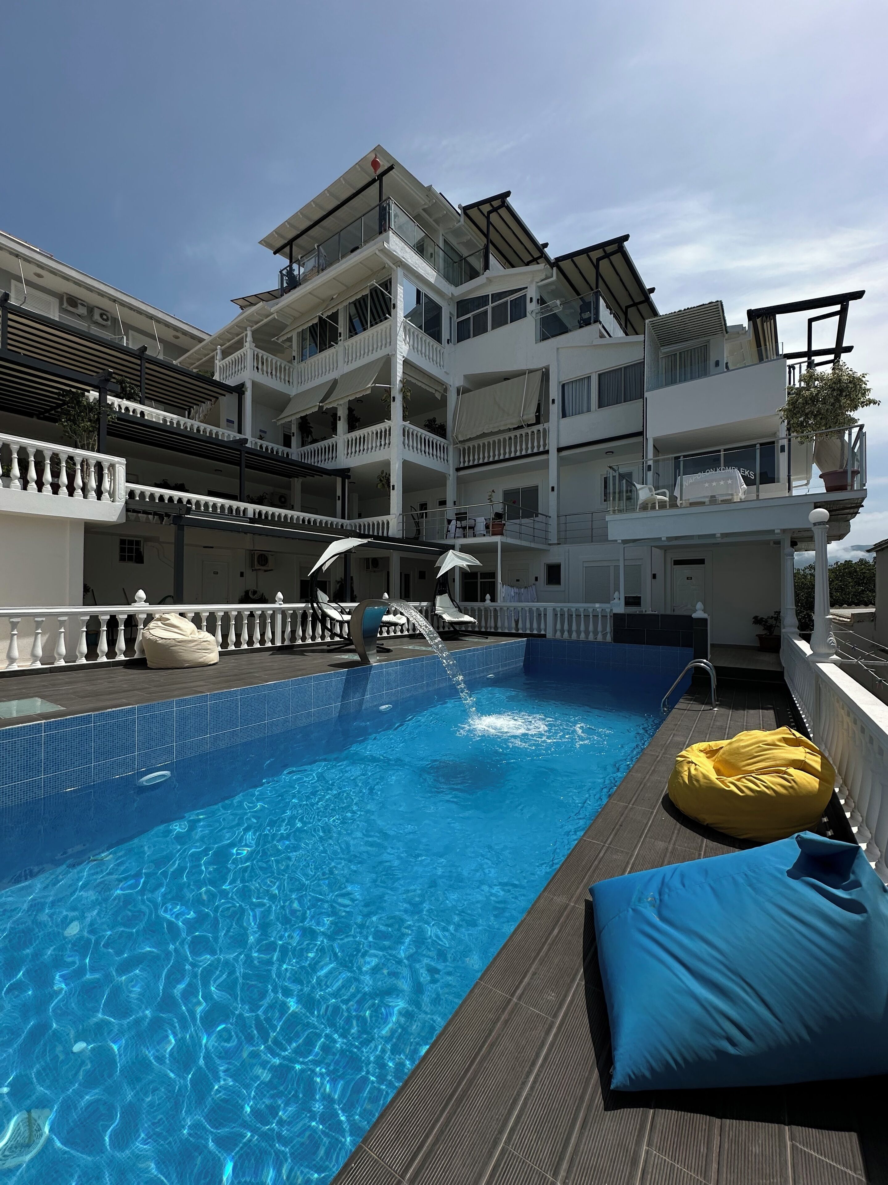 A rooftop swimming pool with a clear blue water surface, surrounded by a wooden deck and white railings.