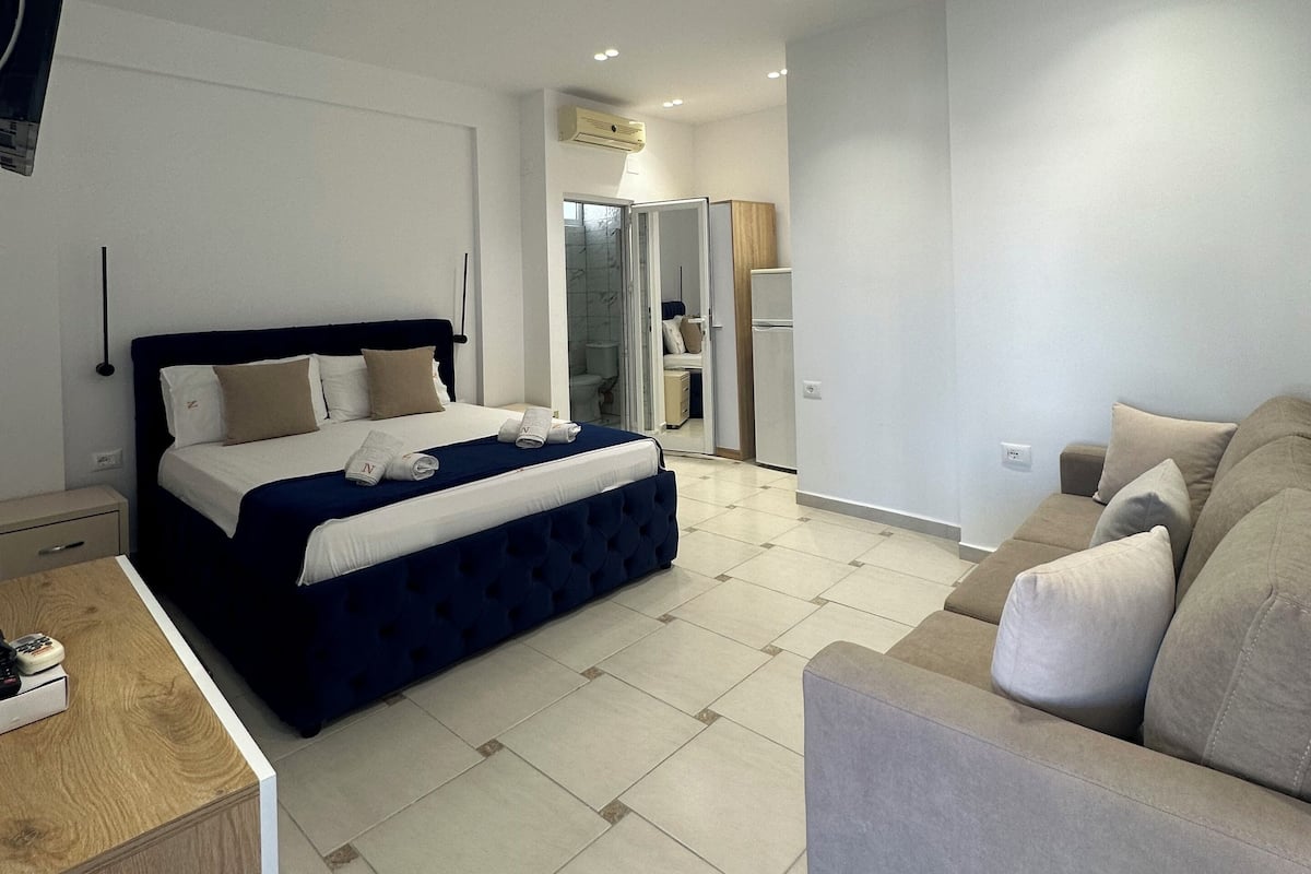 Quarto de hotel moderno com uma cama grande, um sofá e uma mesa pequena.