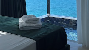 A hotel room with a bed, a view of the sea, and a mountain range in the distance.