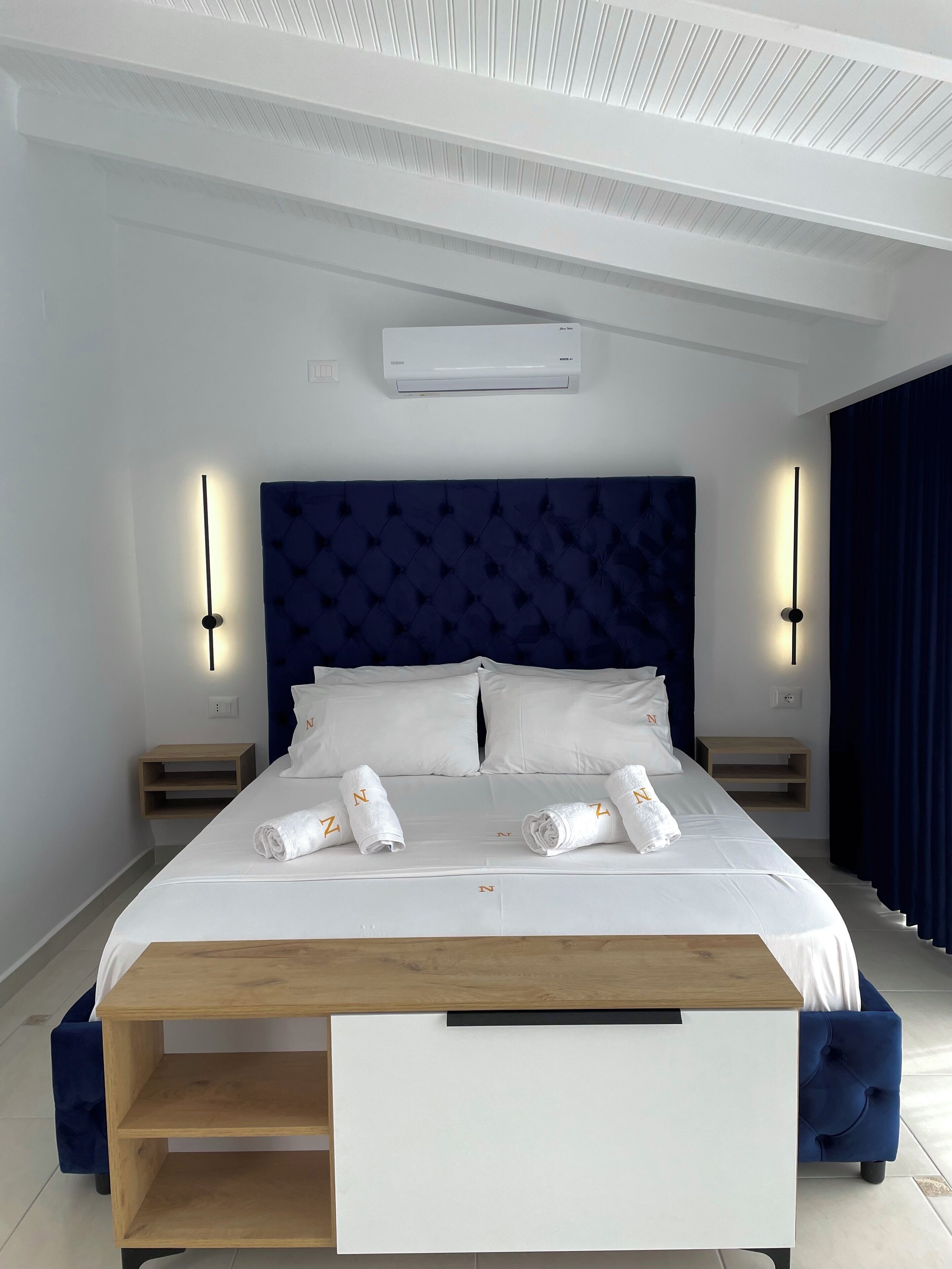 Ein modernes Schlafzimmer mit einem großen Bett, Nachttischen, einer eingebauten Sitzbank und einer Klimaanlage.