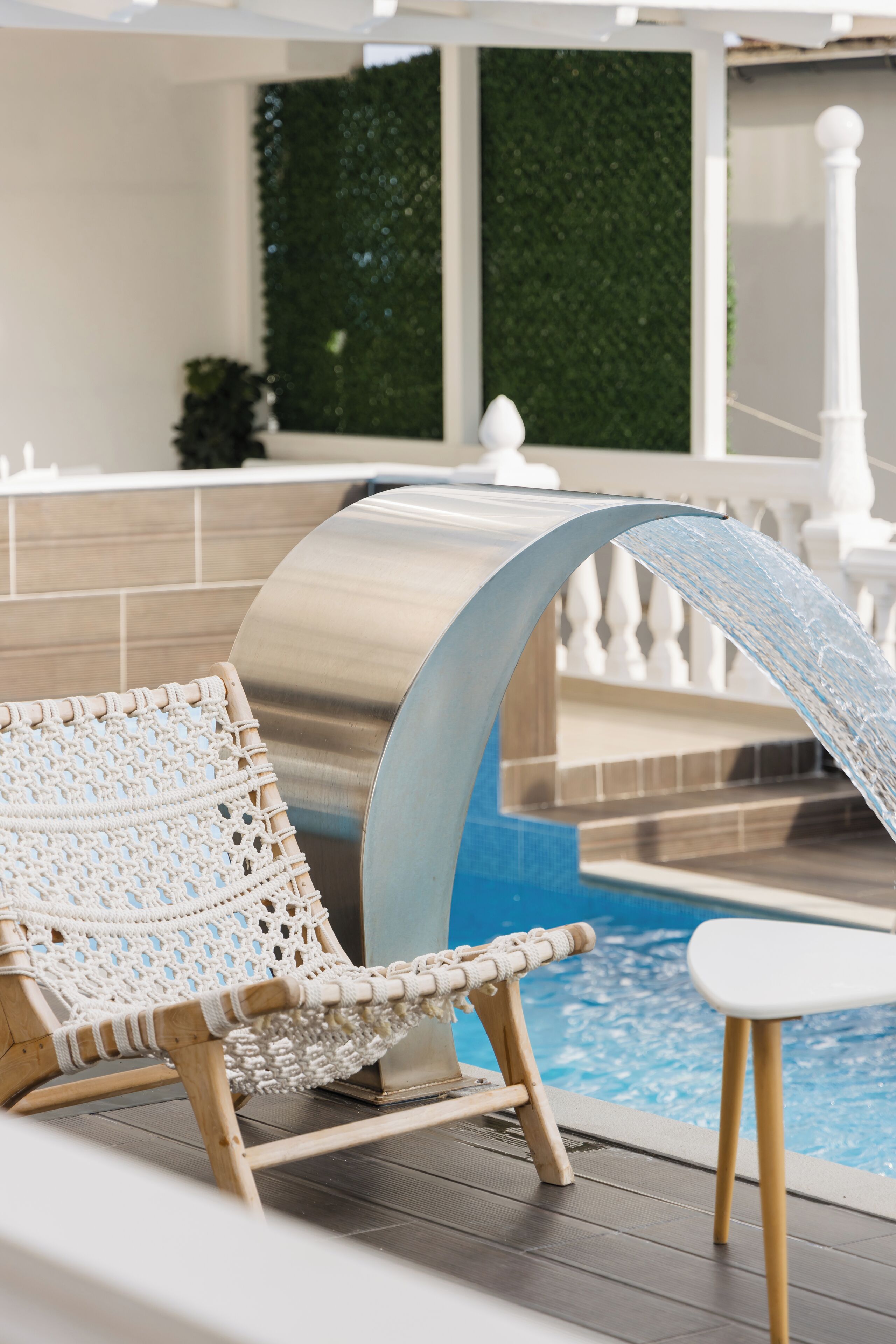 A poolside area with a white chair, a small table, and a water feature.