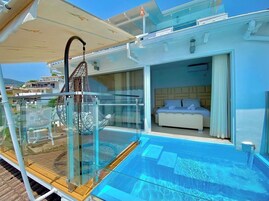 Un balcón con barandilla de vidrio, una piscina y un dormitorio con cama y cortinas.