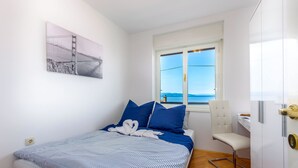 Un dormitorio con cama, una silla, un escritorio, una ventana con vistas y un cuadro en la pared.