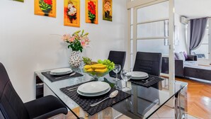 Un comedor con una mesa de vidrio, sillas negras y un jarrón de flores. Cuatro cuadros enmarcados decoran la pared.