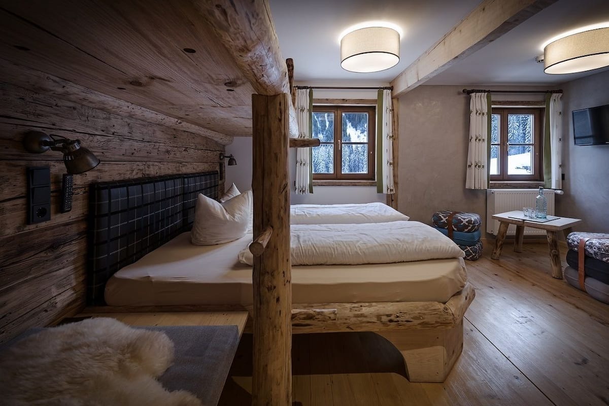 Quarto acolhedor de cabana de madeira com duas camas, cabeceira de madeira, janela com cortinas, uma mesinha e uma televisão.
