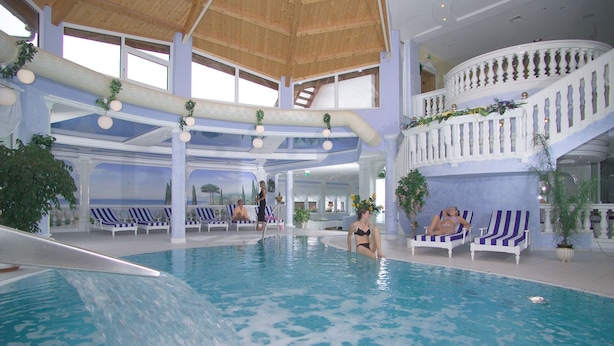 An indoor swimming pool with multiple levels, lounge chairs, and a staircase. - Landgasthof & Hotel Waldow (Guben)