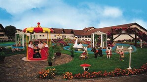 A family enjoying a carousel and a garden area with a fountain and flower beds. - Landgasthof & Hotel Waldow (Guben)