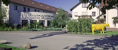 A hotel with a sign reading "Landgasthof Hotel Waldow" and a yellow cow statue in the foreground.