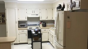 Una cocina compacta con armarios blancos, estufa, microondas y refrigerador.
