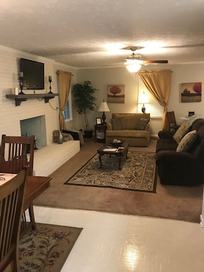 Cozy living room with a fireplace, comfortable seating, and a television, plus a ceiling fan for ventilation.