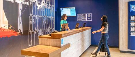 A reception desk with a blue wall and a wooden counter, a digital screen, and a wheelchair accessibility sign.