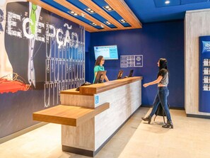 Un comptoir d’accueil avec un mur bleu et un comptoir en bois, un écran numérique et un panneau indiquant que l’établissement est accessible aux personnes en fauteuil roulant.