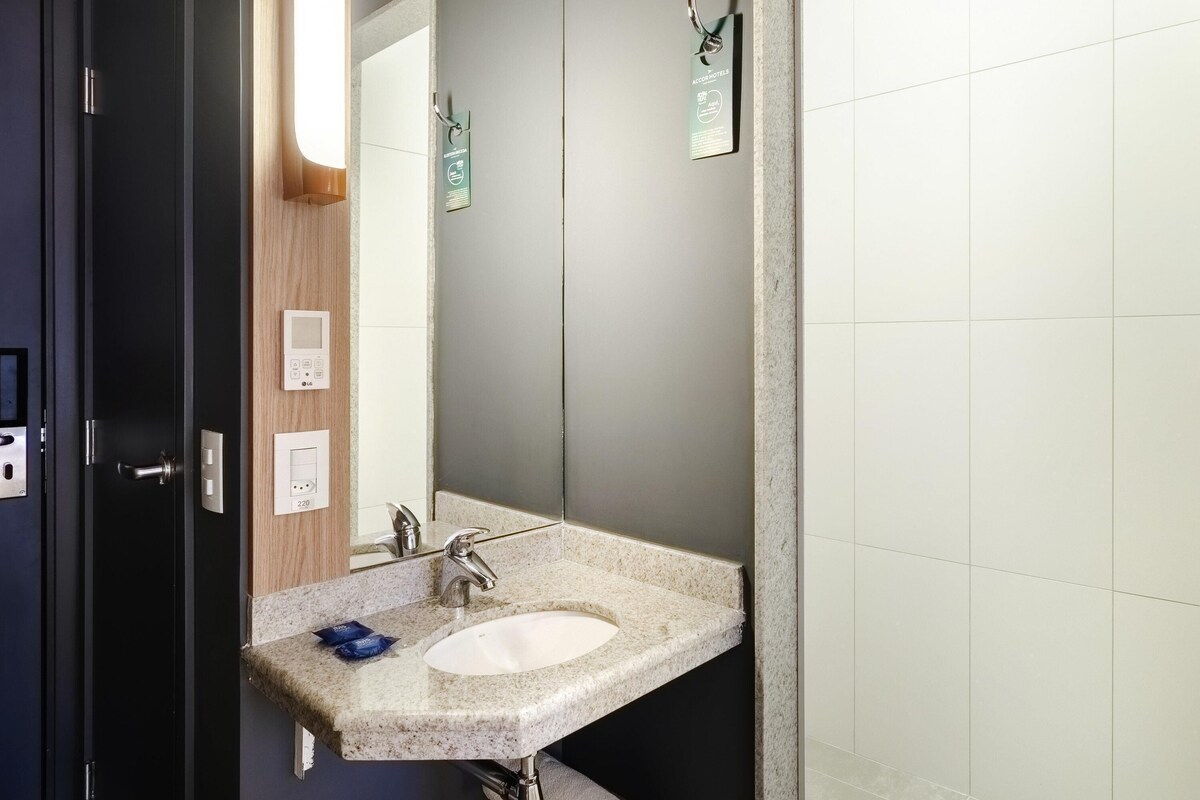 A modern bathroom with a granite sink, a mirror, a towel rack, and a wall-mounted thermostat.