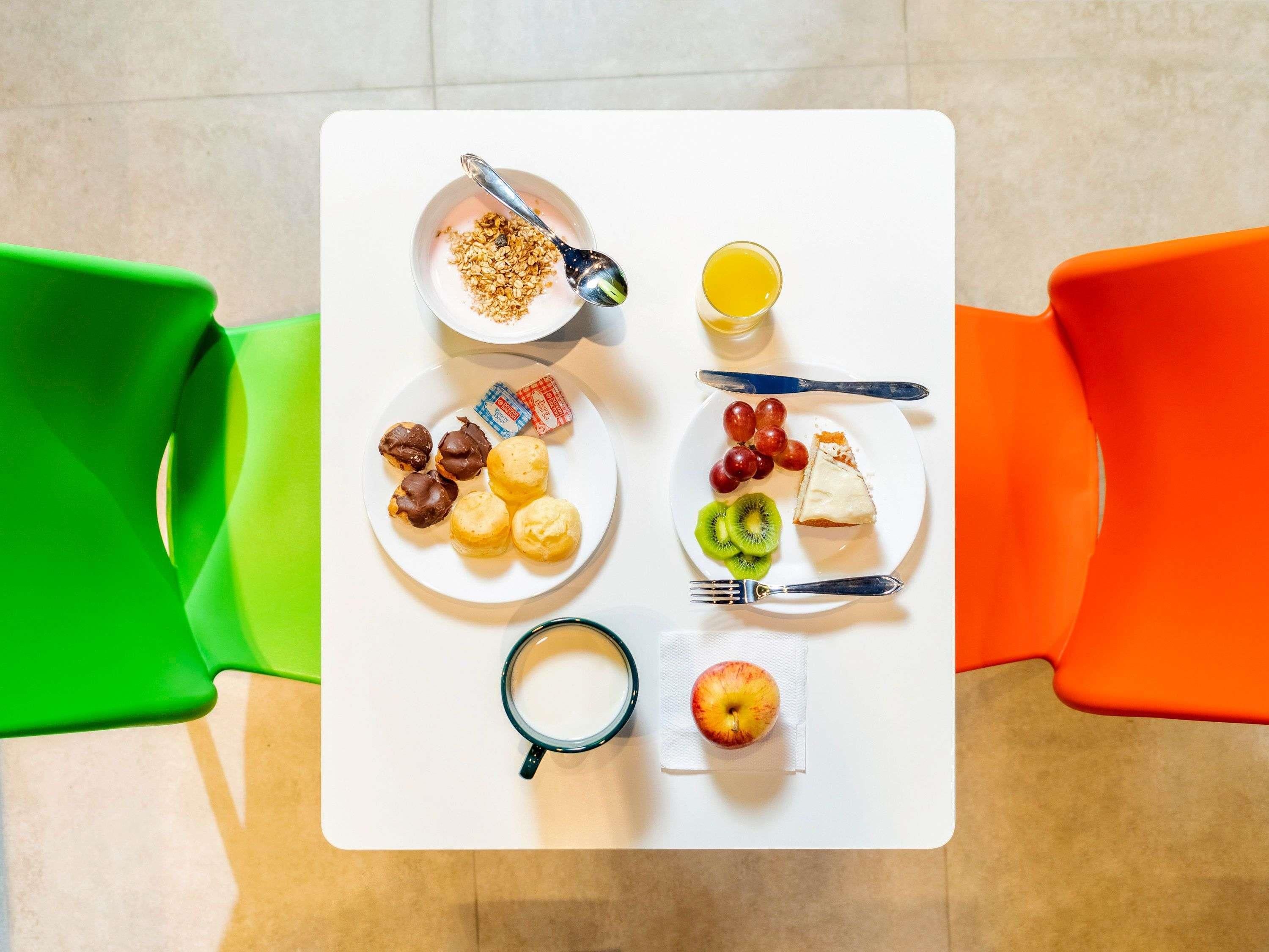 Una mesa con alimentos para el desayuno, como cereales, fruta y bollería, junto con una taza y un vaso de jugo.
