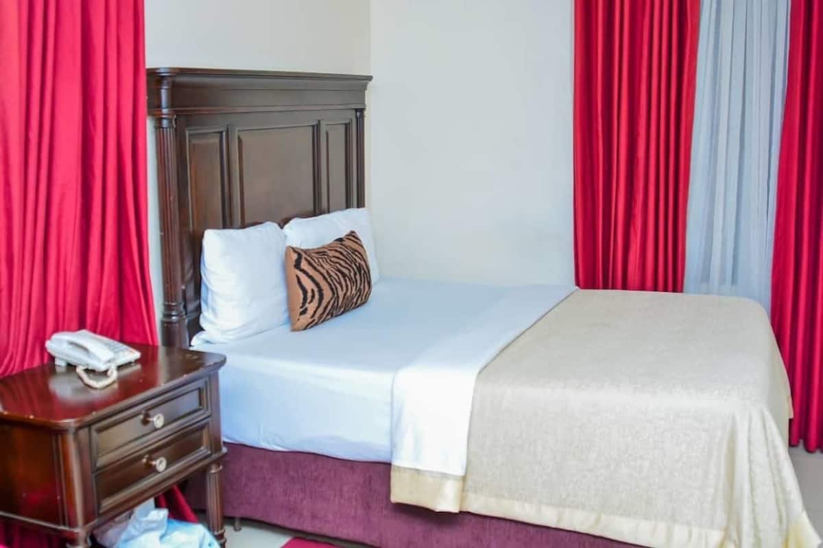 A hotel room with a wooden headboard, a bed with white and beige bedding, a red and white striped pillow, and a bedside table with a telephone.