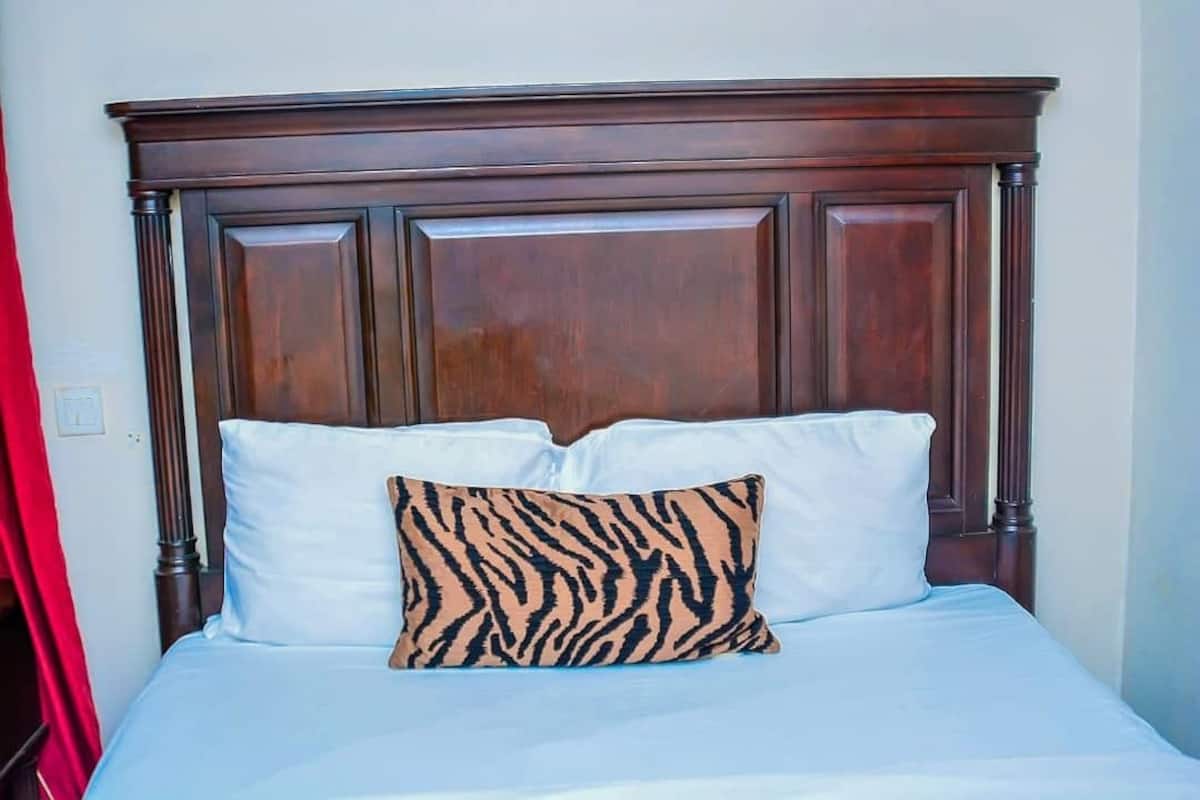 A bed with a wooden headboard, two white pillows, and a single patterned pillow.
