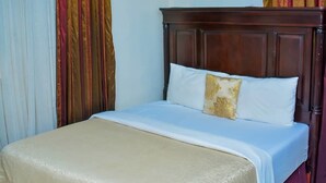 A neatly made bed with a wooden headboard, white bedding, and a decorative pillow. - The Emperor Place Annex (Lagos)