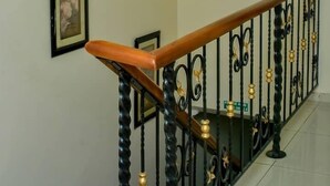 A staircase with a wooden handrail and black balusters, a chandelier with multiple light fixtures, and a framed picture on the wall. - The Emperor Place Annex (Lagos)