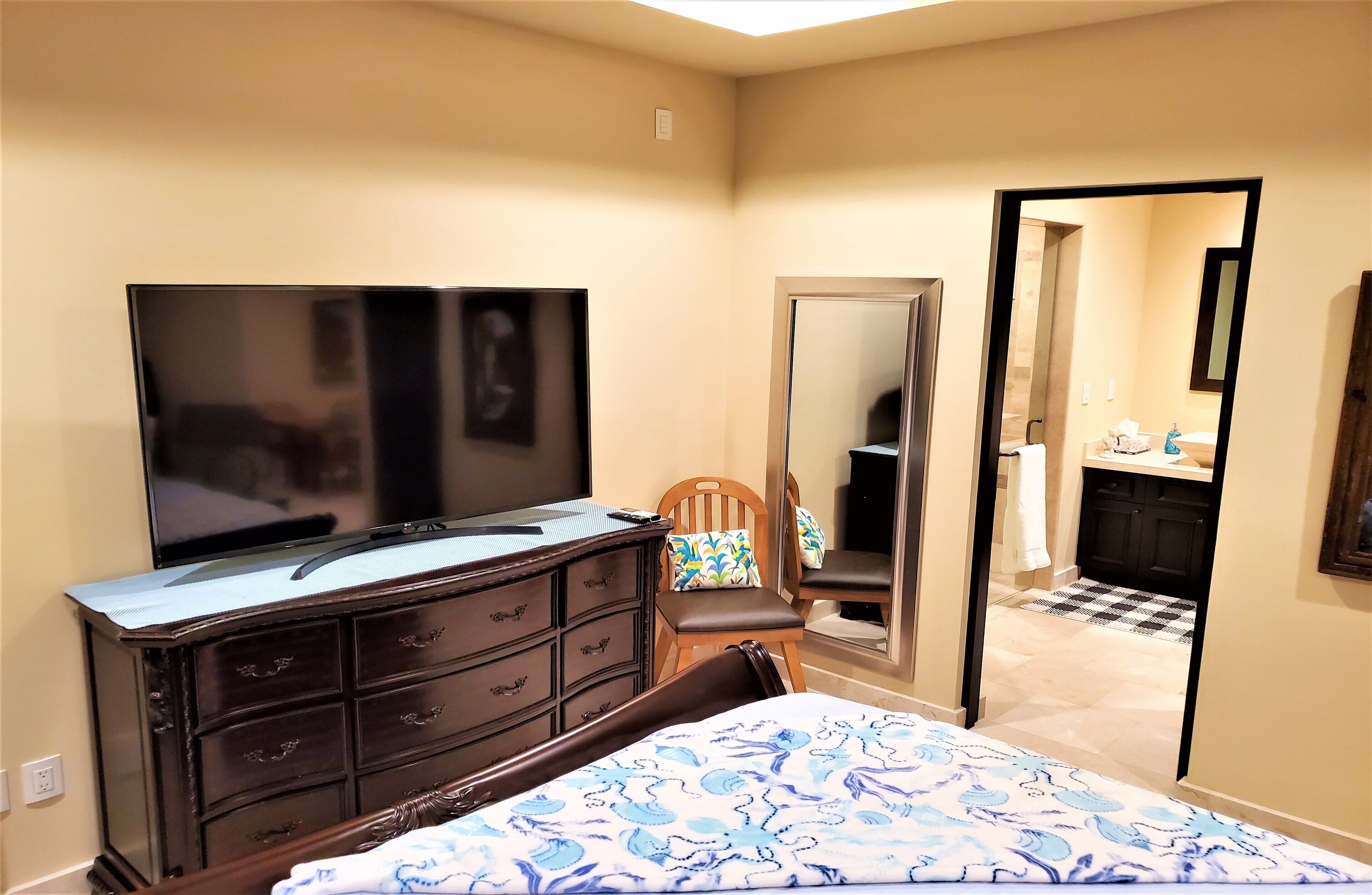 A bedroom with a bed, dresser, TV, chair, and a mirror.