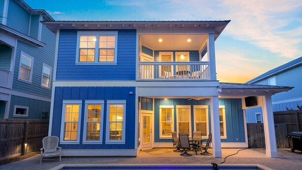 A two-story house with a balcony, a pool, and a patio with outdoor furniture. - Casa Azul - Adorable Home Close to the Beach with Private Pool & Patio! (Miramar Beach)