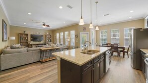 A spacious living area with a large sofa, a dining table, and a kitchen island with a sink. - Casa Azul - Adorable Home Close to the Beach with Private Pool & Patio! (Miramar Beach)