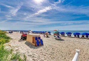 A beach with rows of blue umbrellas and beach chairs, a lifeguard tower, and a pier in the background. - Great beach/golf/winter getaway for the whole family. Winter rentals welcome.  (Myrtle Beach)