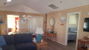 Una sala de estar con un sofá azul oscuro, un otoman a juego y una mesa de centro de madera. Hay una lámpara sobre una mesita auxiliar, un espejo en la pared y un televisor sobre un mueble.