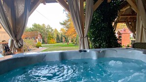 A hot tub under a wooden pergola with curtains, surrounded by a garden and a house in the background. - Willa Wiktoria (Wladyslawowo)