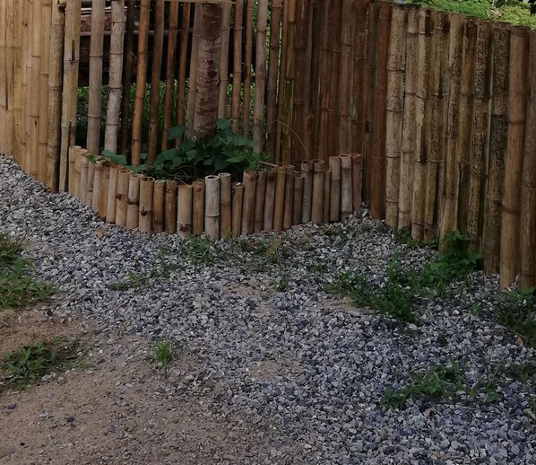 Una cerca de bambú con un camino de grava que lleva a un pequeño jardín.