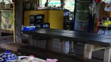 Un área de estar al aire libre de estilo rústico con una mesa y bancos de madera, un refrigerador de Pepsi y un cartel con el menú.