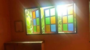 Una habitación con escritorio, taburete, ventana con vidrios de colores e interruptor de luz en la pared.