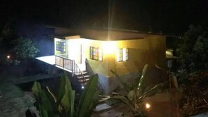Un edificio de dos pisos con un balcón, rodeado de vegetación.