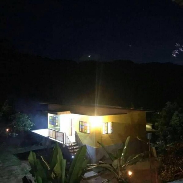 Un edificio de dos pisos con un balcón, rodeado de vegetación.