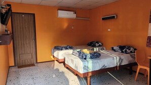 Una habitación con dos camas, una puerta de madera, un aire acondicionado, una mesita y una silla.