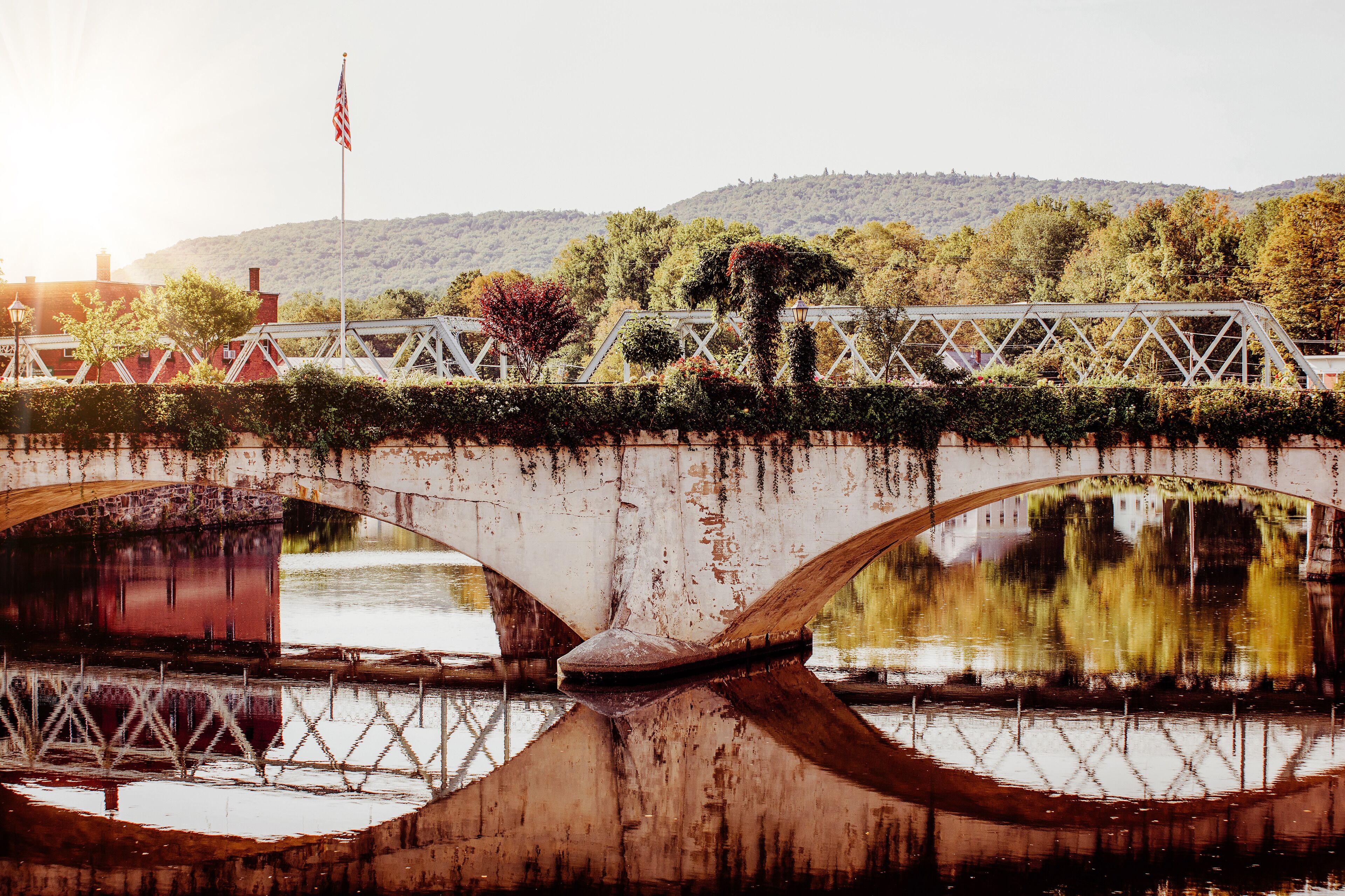 A bridge with a metal truss structure, a flag, and a river below.