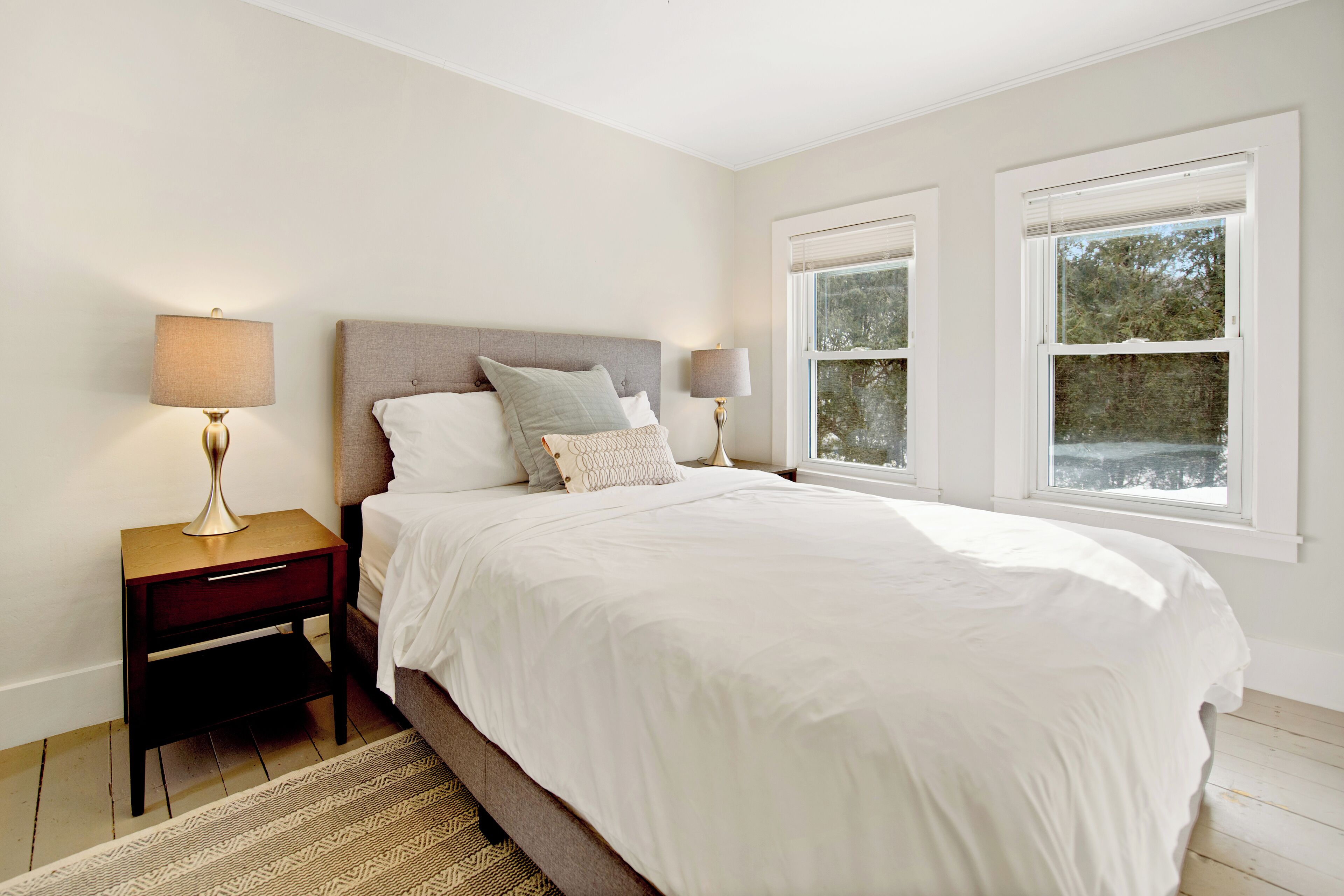 A bedroom with a large bed, two bedside tables, and a window with blinds.