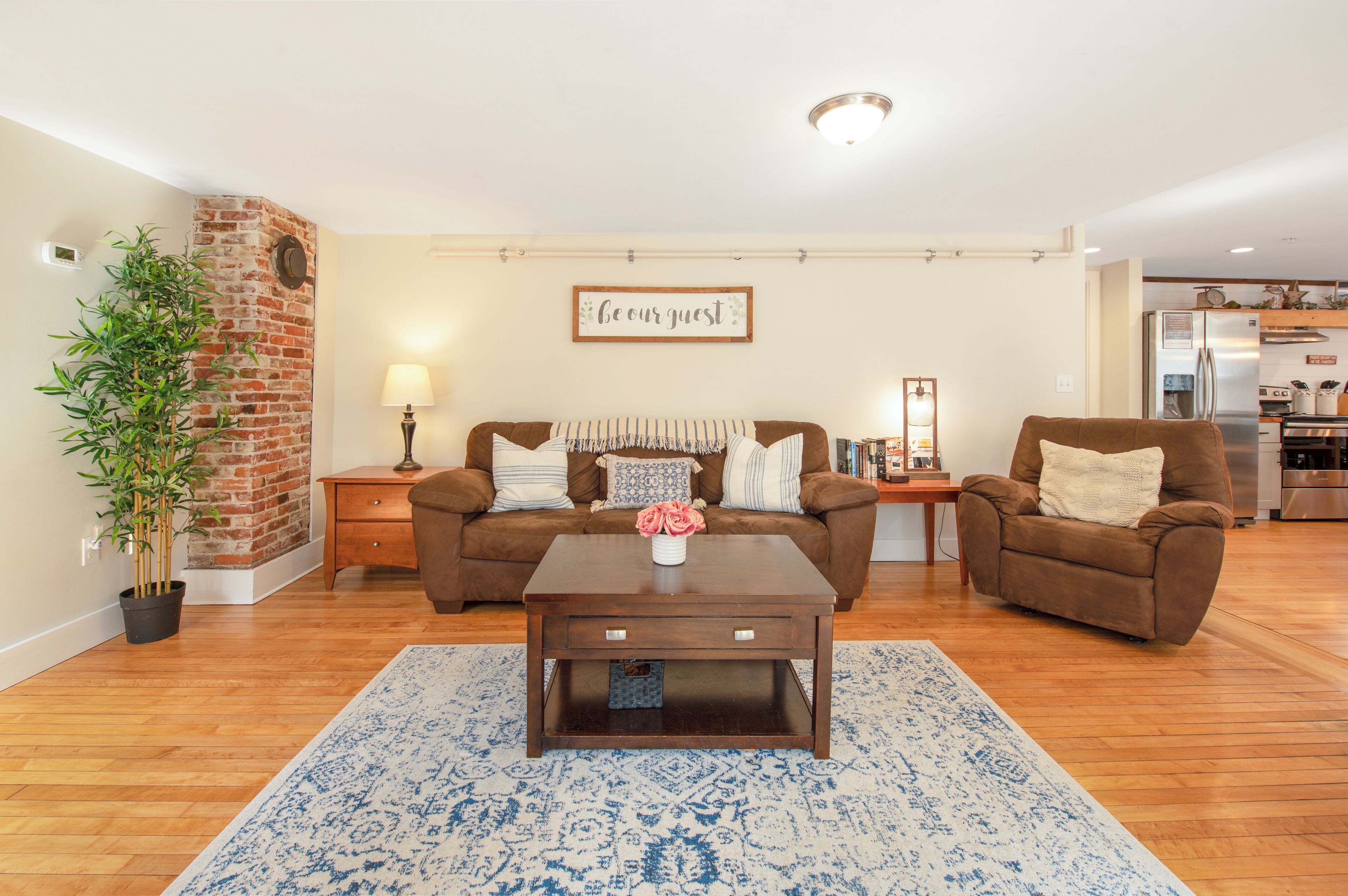 A living room with a brown sofa, a coffee table, and a brick accent wall.
