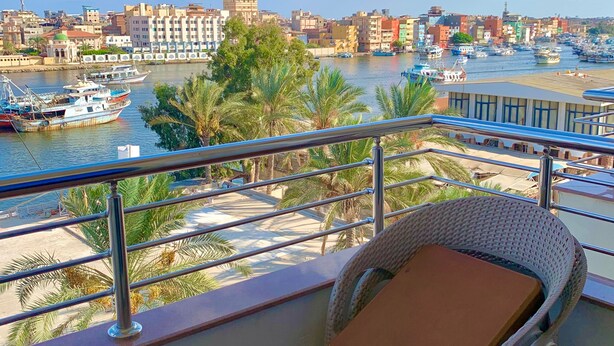 A balcony with a wicker chair, overlooking a harbor with boats and buildings. - Dolphin Ras Elbar (Damietta)