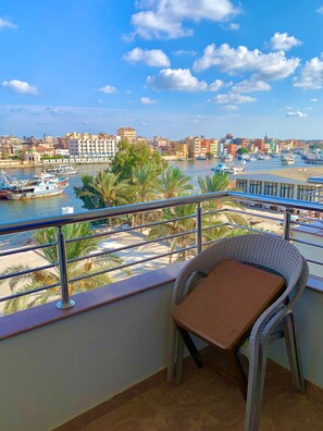 A balcony with a wicker chair, overlooking a harbor with boats and buildings.