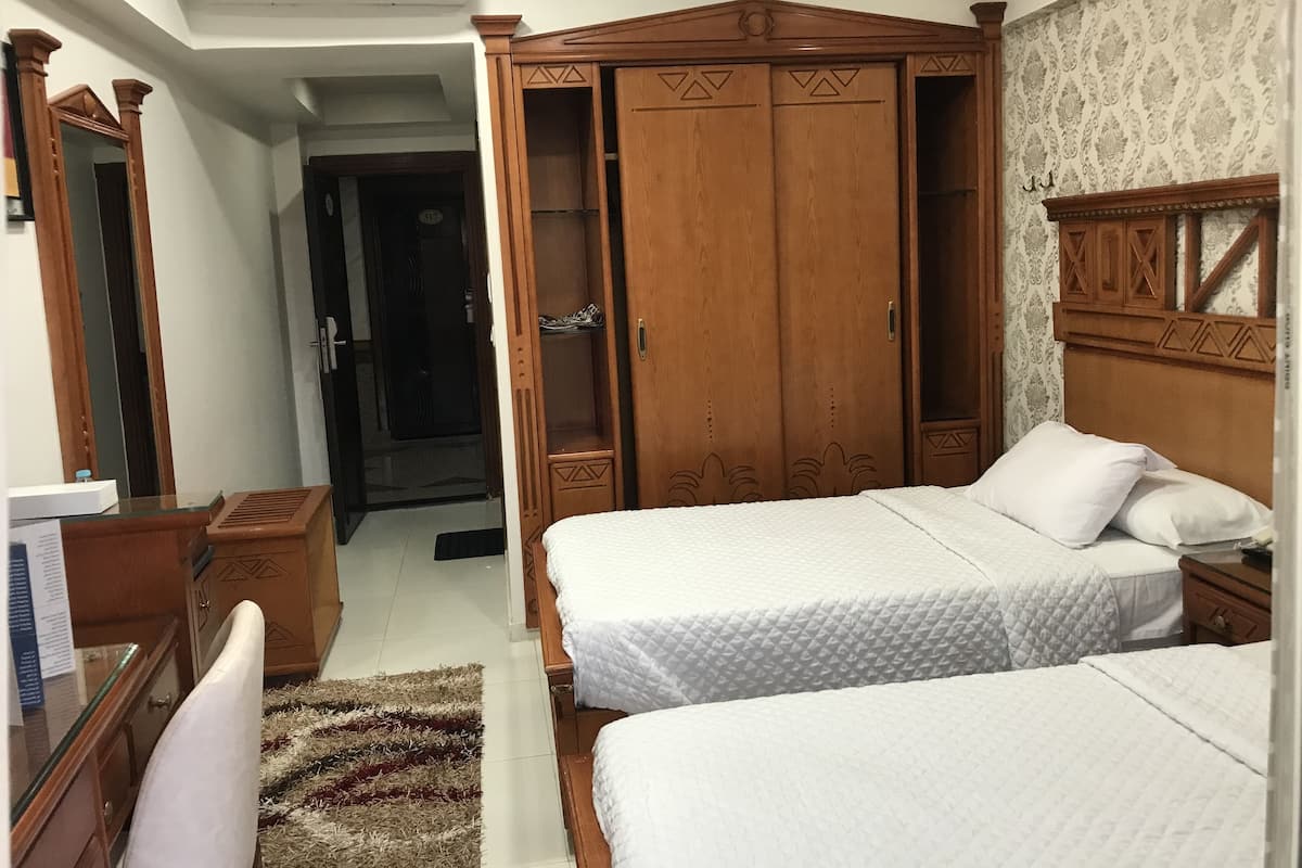 Una habitación de hotel con dos camas, un armario de madera, un espejo y un escritorio pequeño.