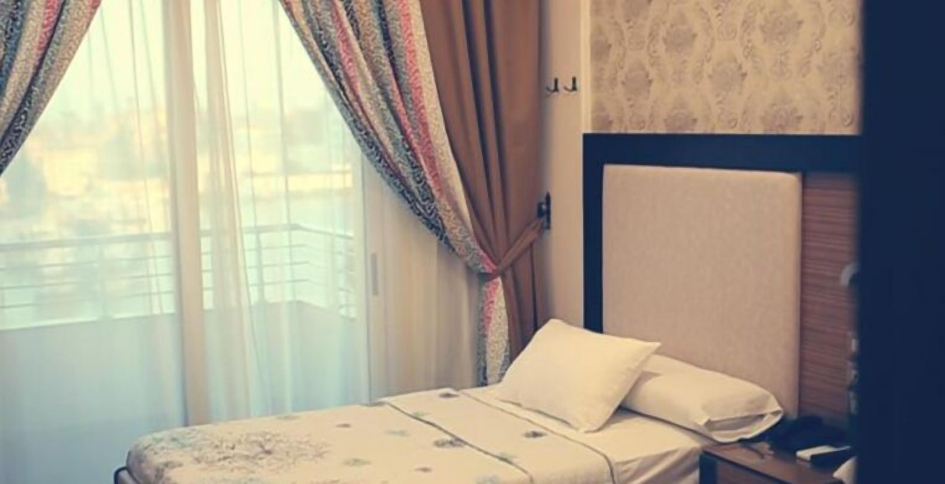 A hotel room with a bed, curtains, and a view of buildings outside.