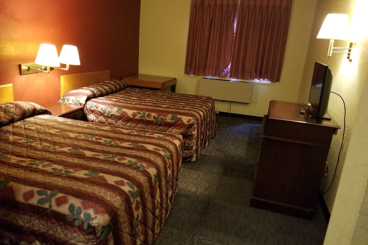 A hotel room with two beds, a desk, a TV, and a window with curtains.