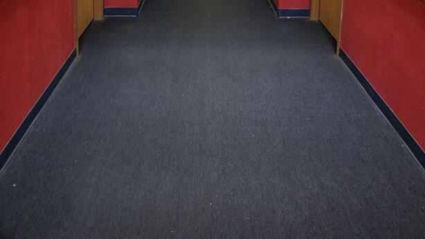 A long, narrow hallway with red and beige walls, carpeted floor, and doors on both sides.