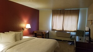 A hotel room with a bed, a desk, a chair, an air conditioner, and a lamp.