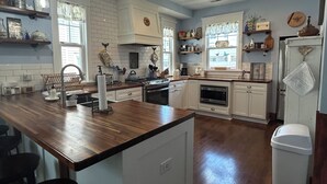 Uma cozinha ampla com armários brancos, uma ilha de madeira e diversos eletrodomésticos.