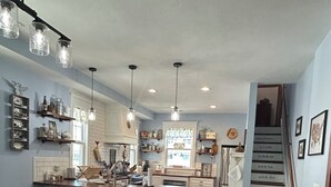 Uma cozinha espaçosa com mesa de jantar de madeira, luminárias pendentes e escada que leva a outro andar.