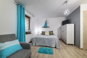 A compact bedroom with a bed, a wardrobe, a grey sofa, a blue curtain, and a chandelier. - Willa w Rozewiu (Wladyslawowo)